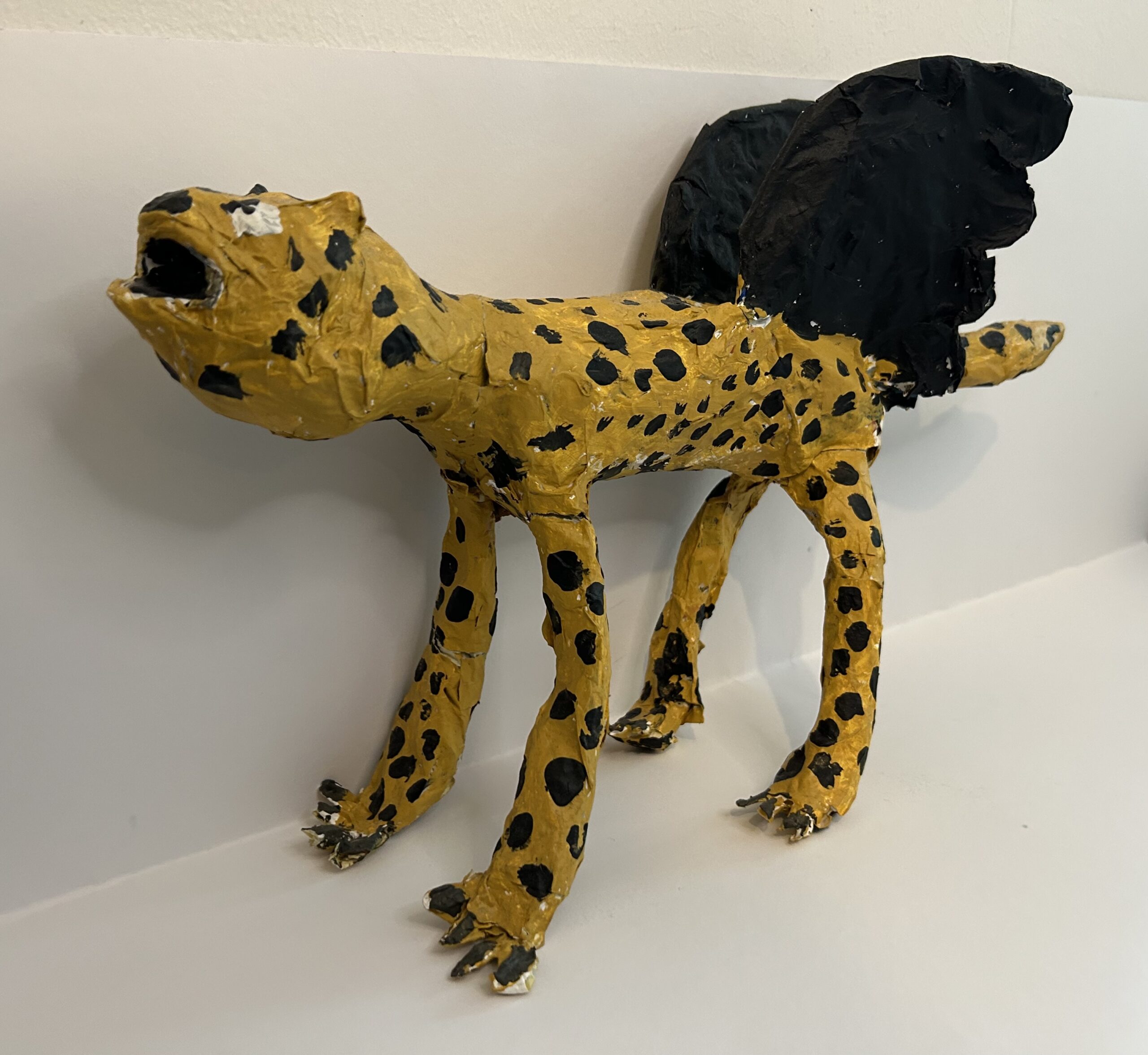 a paper mache mythical leopard-wolf with black bird wings made by a childe